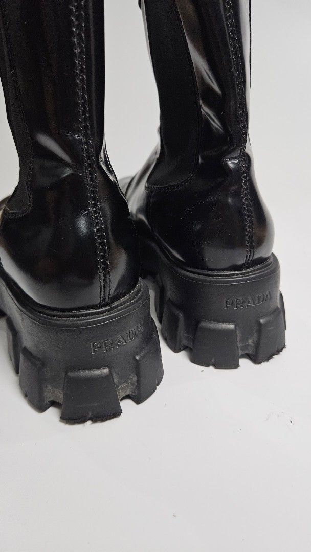 Prada Monolith Brush Leather Chelsea Boots (Category: Boots) located in Alfonso. Submitted by jbcamet (Listing ID 1467325080, Image 2). Description: - Color: Glossy black brushed leather - Signature chunky lug sole with debossed Prada logo - Iconic enameled metal triangle logo on the shaft - Convenient pull tabs and elastic side gussets - Made in Italy - Condition: Normal wear on uppers and soles from regular use - Perfect for elevating any stree