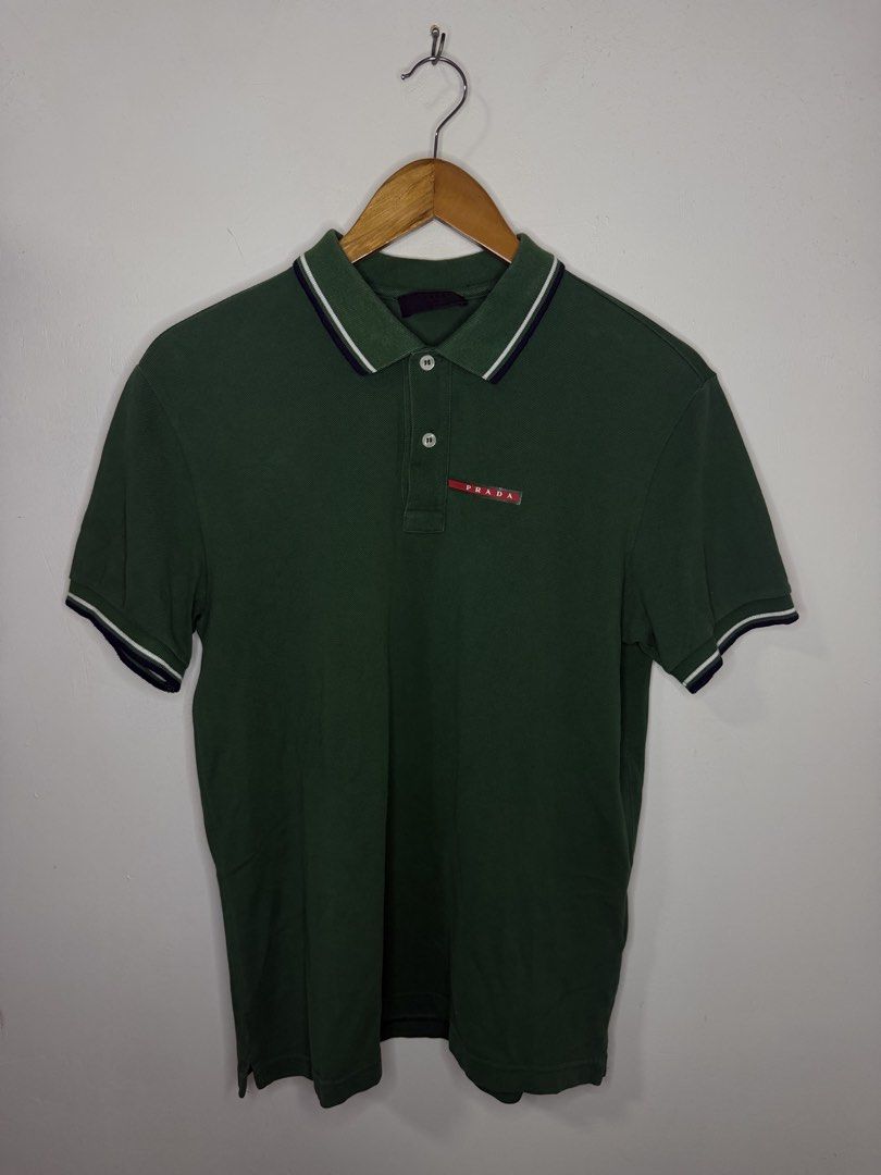 Prada Polo Shirt (Green) (Category: Tshirts & Polo Shirts ) located in Manila. Submitted by jcarchives14 (Listing ID 1467277665, Image 1). Description: - Brand: Prada - Color: Dark green with white and navy collar/cuff tipping - Details: Red Prada rubber logo patch on chest, 2-button placket - Fit: Classic fit, short sleeves - Condition: Clean and ready to wear - Note: Measurements available upon request.