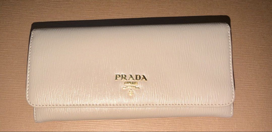 Prada Saffiano Leather Long Wallet Beige (Category: Wallets & Card holders) located in Marikina City. Submitted by owen_goldsmith (Listing ID 1467305259, Image 1). Description: - Brand: Prada - Style: Long wallet - Material: Beige textured leather with clean edges and minimal wear - Hardware: Gold lettering on the front flap - Closure: Secure snap closure - Features: Compartments for cards, cash, and coins - Color: Neutral beige that matches any 