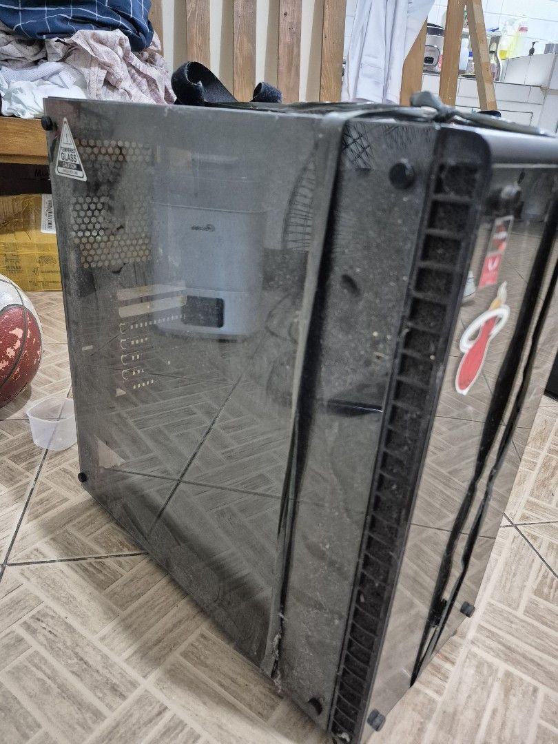 RAKK Tempered Glass Pc Case (Category: Computer Parts) located in Manila. Submitted by trstnkm (Listing ID 1467253170, Image 2). Description: - Tempered glass panels on the side and front - Customized front glass with gaming & sports stickers (HyperX, ASUS ROG, Miami Heat) - Top I/O panel equipped with power button, audio jacks, and USB ports - Condition: Some dust on top vent and panels; currently held together with grey strapping tape - Include