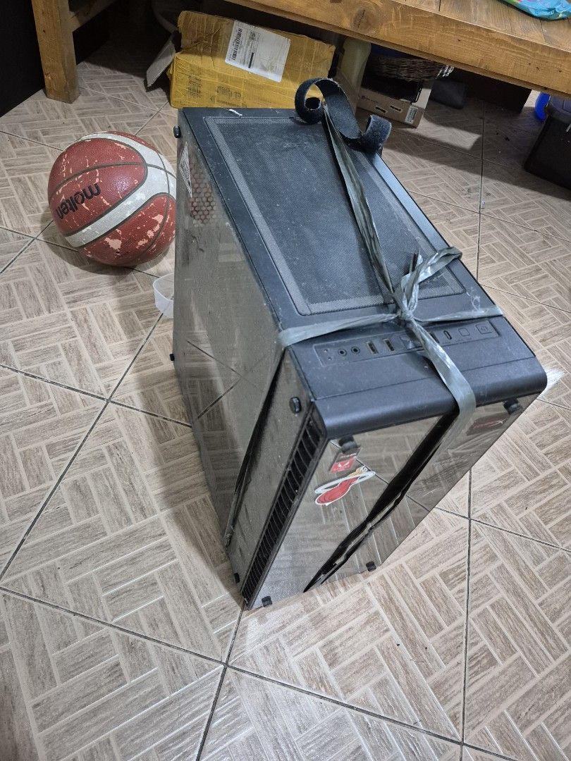 RAKK Tempered Glass Pc Case (Category: Computer Parts) located in Manila. Submitted by trstnkm (Listing ID 1467253170, Image 3). Description: - Tempered glass panels on the side and front - Customized front glass with gaming & sports stickers (HyperX, ASUS ROG, Miami Heat) - Top I/O panel equipped with power button, audio jacks, and USB ports - Condition: Some dust on top vent and panels; currently held together with grey strapping tape - Include