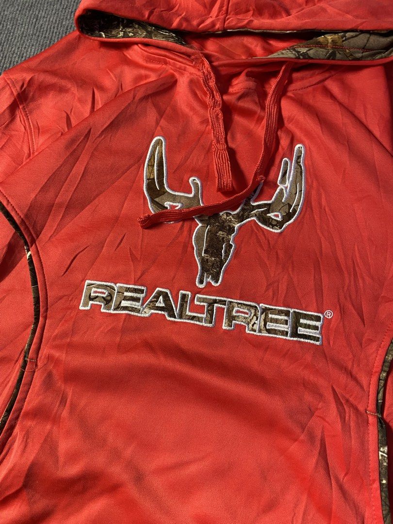 Realtree pink Camo Accent Pullover Hoodie (Category: Coats, Jackets and Outerwear) located in Maria Aurora. Submitted by mightypenguin.f7ca53 (Listing ID 1467272794, Image 2). Description: - Brand: Realtree - Color: Bright orange with camo accents - Design: Embroidered antler logo on chest, camo hood lining and pocket trims - Features: Adjustable drawstrings, front kangaroo pocket - Material: Soft fabric construction.