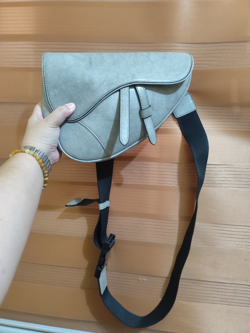 River Stone Grey Saddle Crossbody Bag (Category: Cross-body Bags) located in Naga. Submitted by semflewer (Listing ID 1467344752, Image 1). Description: - Brand: River Stone - Color: Grey with a cool distressed finish look - Design: Asymmetric flap with stylish decorative straps - Closure: Secure zip-top opening underneath the main flap - Strap: Thick, adjustable black strap with a buckle closure - Interior: Black fabric lining with a built-in zi