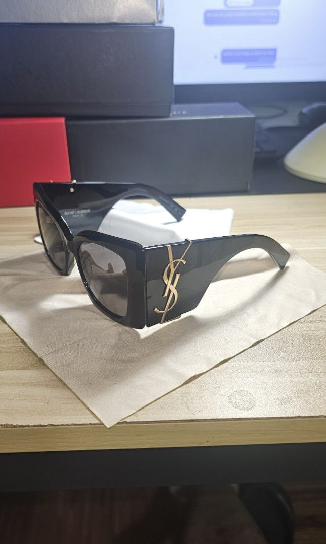 Saint Laurent Sunglasses with YSL Monogram Black (Category: Sunglasses & Eyewear) located in Manila. Submitted by anthonylee23810 (Listing ID 1466449749, Image 1). Description: Black frames with dark tinted lenses. Gold YSL monogram logo on the temples. Thick arm design. Includes a Dolce & Gabbana box and dust pouch. Box shows minor wear. Clean lenses and frames overall. Ready to wear..