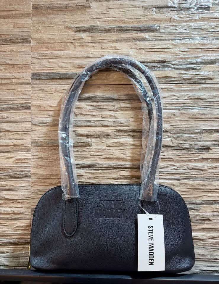Steve Madden Black Shoulder Bag (Category: Shoulder Bags) located in Manila. Submitted by renee_12 (Listing ID 1467317340, Image 1). Description: - Brand: Steve Madden - Color: Classic Black - Material: Textured leather with a sleek, structured shape - Handles: Dual top handles, still wrapped in original protective plastic - Closure: Secure top zip closure - Details: Chic embossed logo on the front - Condition: Brand new with original retail tag 