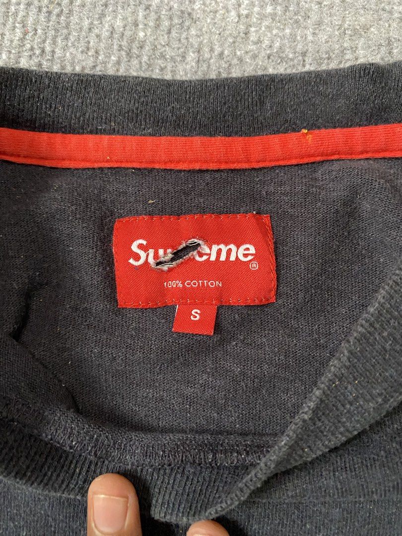 Supreme Black Pocket Tee (Category: Tshirts & Polo Shirts ) located in Maria Aurora. Submitted by mightypenguin.f7ca53 (Listing ID 1467273866, Image 3). Description: - Brand: Supreme - Color: Black with red inner collar detail - Features: Chest pocket and iconic streetwear design - Size: S (tag attached at neckline) - Condition: Slight fabric fading from wear; minor fraying visible on the brand label.