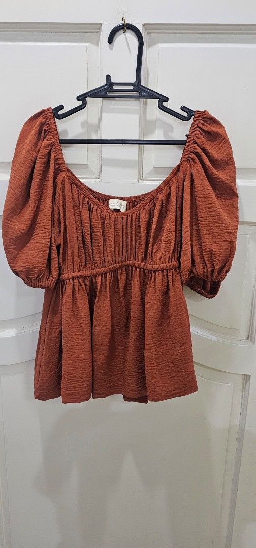 TAYO STUDIO Rust Orange Puff Sleeve Top Size 2 (Category: Blouses) located in Davao. Submitted by sachigo (Listing ID 1467261443, Image 2). Description: - Brand: KYD Studio - Size: 2 - Color: Rust / Earthy burnt orange - Design: Square neckline, gathered shirred bodice, short puff sleeves, flared peplum hem - Fabric: Textured with a slight crinkle effect - Condition: Excellent, easy to match with denim or skirts used 1 hr only by the model.