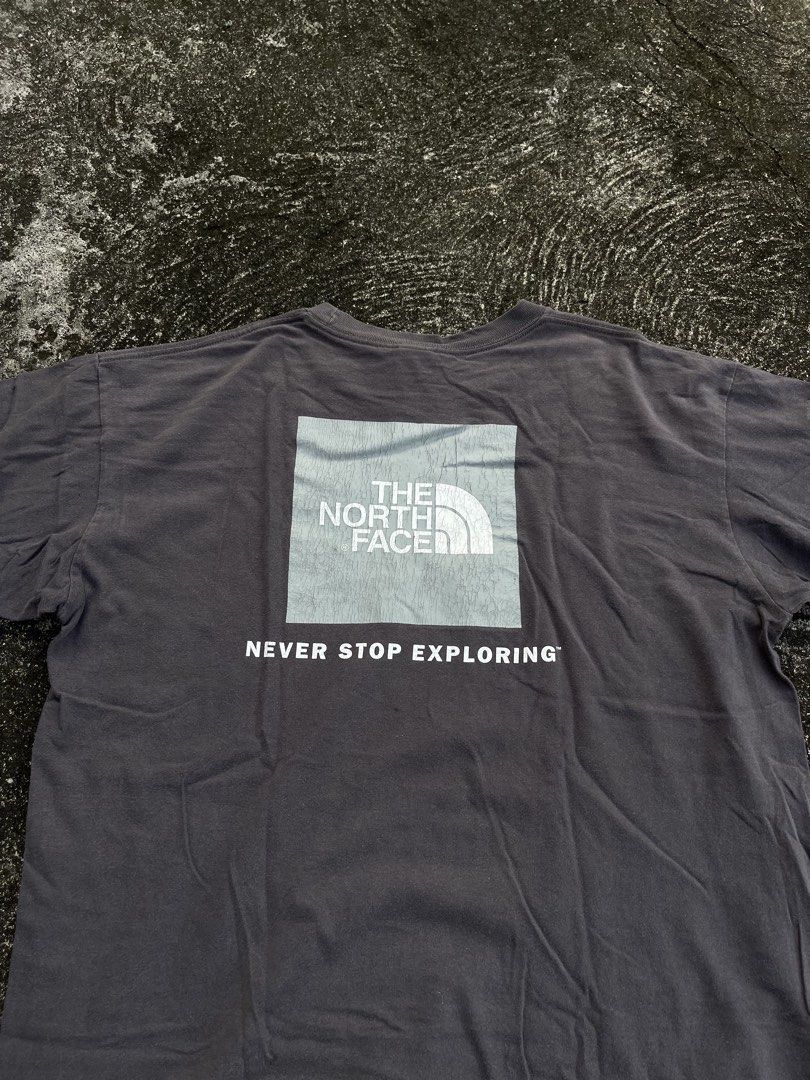 The North Face Never Stop Exploring T-Shirt (Category: Tshirts & Polo Shirts ) located in Tarlac. Submitted by supremo.0 (Listing ID 1467173638, Image 2). Description: - Brand: The North Face - Color: Dark grey with a cool washed-out fade - Size: Men's Large (Made in El Salvador) (23.5x28) - Design: Small chest logo on front, large box logo graphic with 'Never Stop Exploring' on the back - Material: Comfortable cotton fabric - Fit: Crew neck, sho