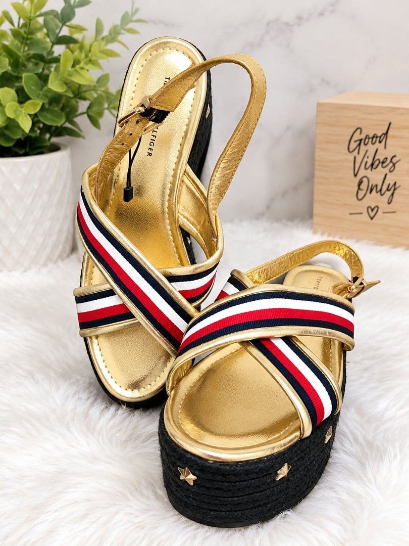 Tommy Hilfiger Gold Platform Wedge Sandals (Category: Wedges) located in Lucena. Submitted by amirahsoonlineshop (Listing ID 1467355368, Image 1). Description: Tommy Hilfiger platform wedge sandals in metallic gold. Signature red, white, and navy striped crossover fabric straps. Black woven espadrille wedge heel decorated with small star studs along the base. Adjustable ankle strap with buckle closure. Size 39 EUR / 8.5 US..