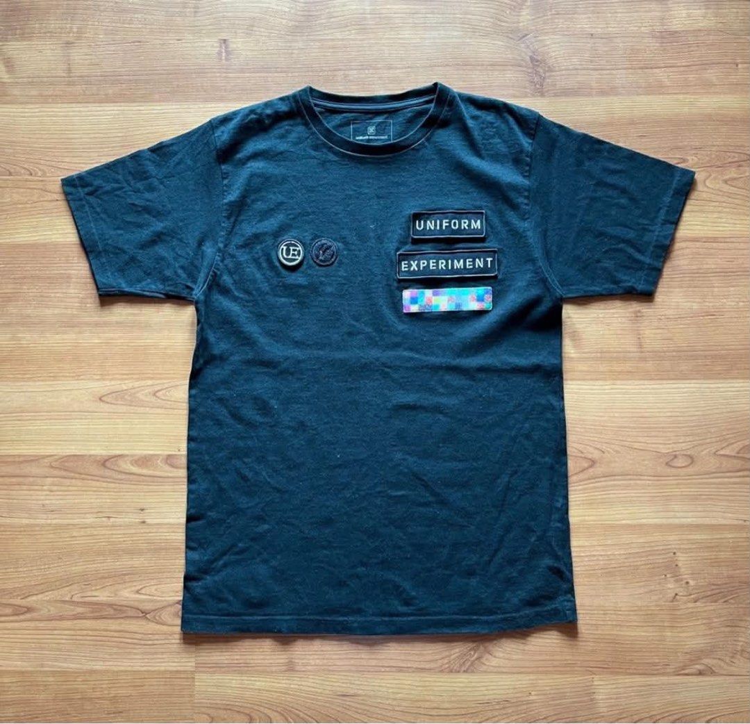Uniform Experiment Shirt (Category: Tshirts & Polo Shirts ) located in Rizal. Submitted by timelessfinds89_ (Listing ID 1467314302, Image 1). Description: - Brand: Uniform Experiment - Color: Black - Size: Tagged size 3 - Design: Embroidered "UNIFORM EXPERIMENT" and circular logo patches on chest - Details: Colorful pixelated graphic tags near the hem and lower back - Condition: Slight signs of wear along the neckline Condition : good condish Siz