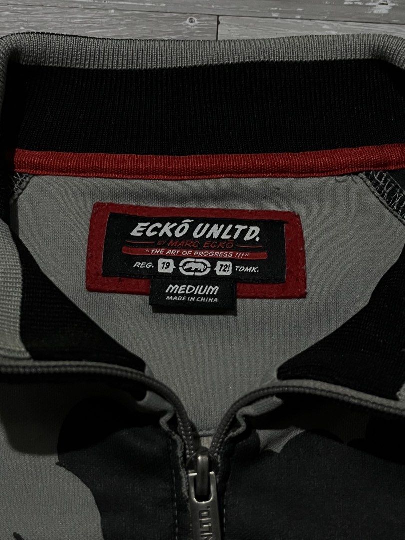 VINTAGE ECKO TRACK JACKET (Category: Coats, Jackets and Outerwear) located in Manila. Submitted by randomloots2 (Listing ID 1467291085, Image 3). Description: - Brand: Marc Ecko - Size: Medium - Color: Black, grey, and white - Design: Bold comic book graphic print with 'Ecko Unlimited!!!' embroidery - Details: Full front zipper with branded metal pull, striped ribbed collar, cuffs, and hem - Condition: Inner neck label and care instructions attac