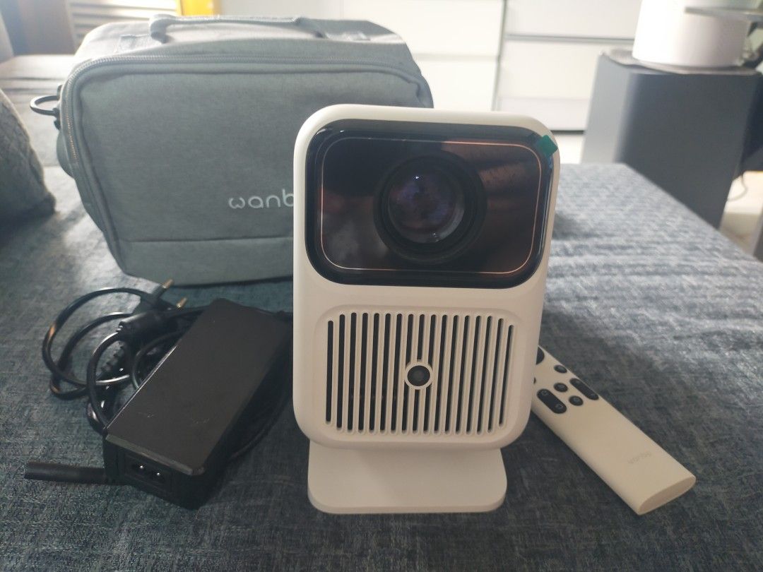 Wanbo Projector with Carry Bag and Remote (Category: Projectors) located in Quezon City. Submitted by ckxhermoso (Listing ID 1467184779, Image 1). Description: - Model: Wanbo portable projector in clean white - Condition: Fully functional and ready to use - Includes: Power adapter, remote control, and a matching grey carry bag with a strap - Ports: Equipped with HDMI and USB ports on the back panel - Design: Compact upright build with front lens 
