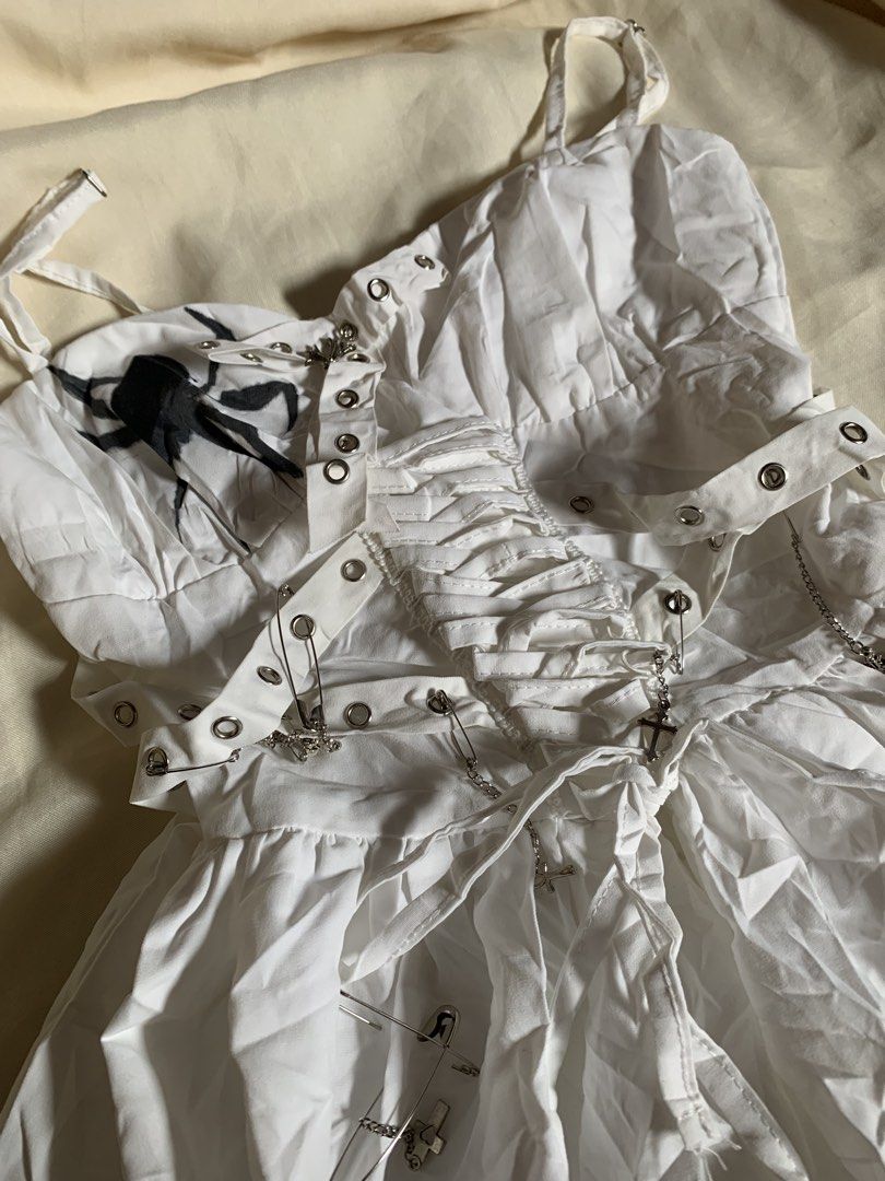 White Alternative Goth Spider Flame Corset Dress (Category: Dresses) located in Davao. Submitted by cheineebau09680 (Listing ID 1467210950, Image 2). Description: - Style: White alternative mini dress - Size: Small - Material: 100% polyester - Details: Spider graphic near neckline, flame print along the hem - Back: Lace-up corset back with grommets and straps - Accents: Silver safety pins and hanging cross charms with chains - Care: Hand wash onl