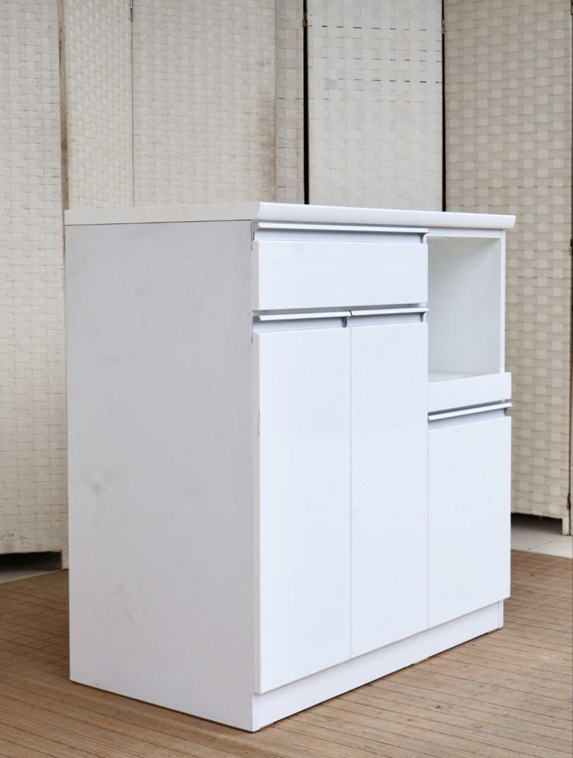 White kitchen storage cabinet with drawers and open shelf (Category: Shelves, Cabinets & Racks) located in Bulacan. Submitted by FurnitureGallery (Listing ID 1467306905, Image 3). Description: - Color & Finish: Clean modern white - Storage: 1 top drawer, left double-door cabinet, and right lower cabinet - Microwave Space: Open compartment with a built-in power outlet for easy plugging - Surface: Solid countertop, perfect for prep or appliances - 