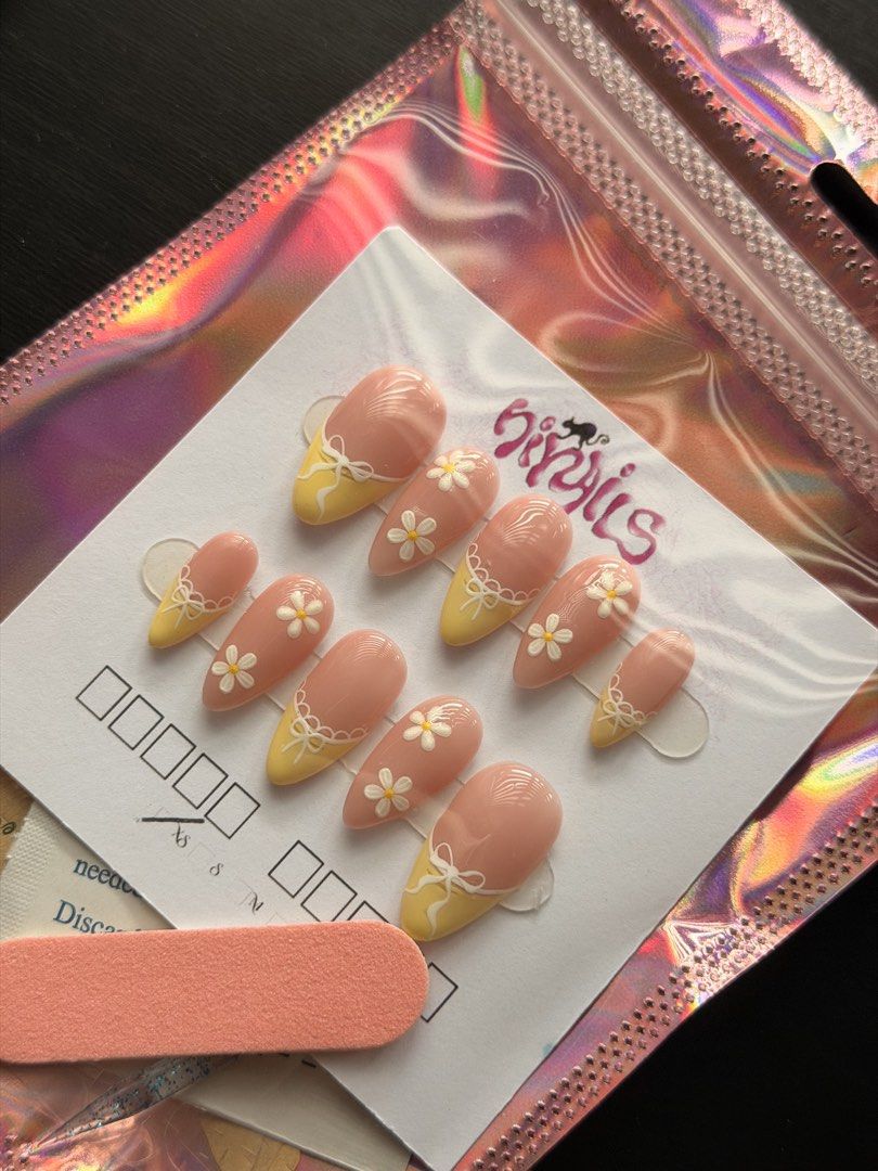 Yellow Daisy Bow Press On Nails (SIZE XS) (Category: Hands & Nails) located in Quezon City. Submitted by ninny.ph (Listing ID 1467190921, Image 1). Description: - Brand: HiyNails (Handmade press-on nails) - Design: Almond shape, soft pink base, yellow tips, white daisies, and 3D bow accents - Inclusion: Full set of 10 nails on a display card - Freebies: Mini nail file and prep wipe included - Packaging: Iridescent holographic storage pouch - Cond