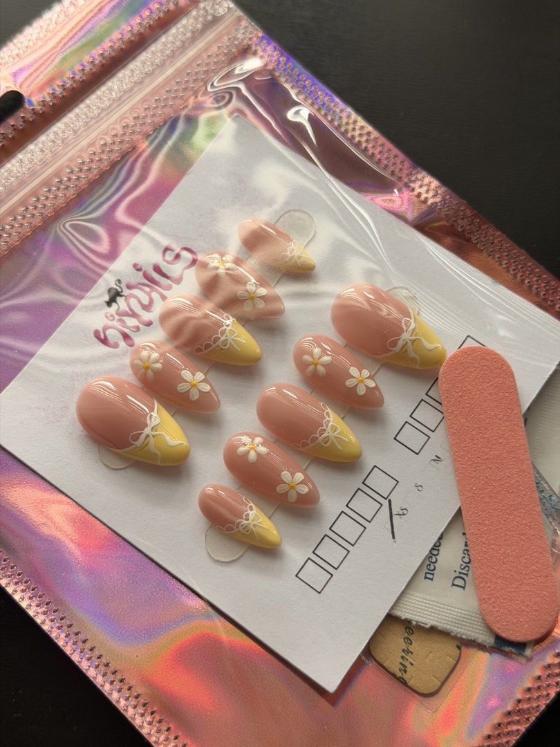 Yellow Daisy Bow Press On Nails (SIZE XS) (Category: Hands & Nails) located in Quezon City. Submitted by ninny.ph (Listing ID 1467190921, Image 2). Description: - Brand: HiyNails (Handmade press-on nails) - Design: Almond shape, soft pink base, yellow tips, white daisies, and 3D bow accents - Inclusion: Full set of 10 nails on a display card - Freebies: Mini nail file and prep wipe included - Packaging: Iridescent holographic storage pouch - Cond