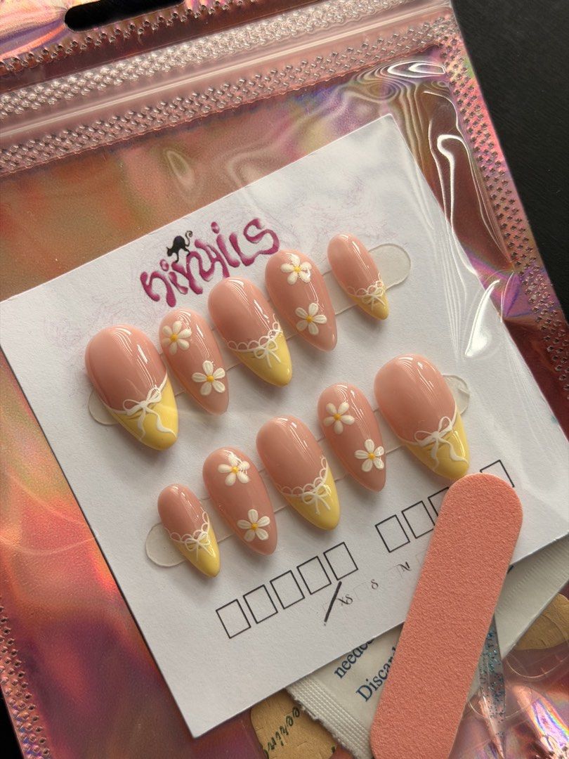 Yellow Daisy Bow Press On Nails (SIZE XS) (Category: Hands & Nails) located in Quezon City. Submitted by ninny.ph (Listing ID 1467190921, Image 3). Description: - Brand: HiyNails (Handmade press-on nails) - Design: Almond shape, soft pink base, yellow tips, white daisies, and 3D bow accents - Inclusion: Full set of 10 nails on a display card - Freebies: Mini nail file and prep wipe included - Packaging: Iridescent holographic storage pouch - Cond