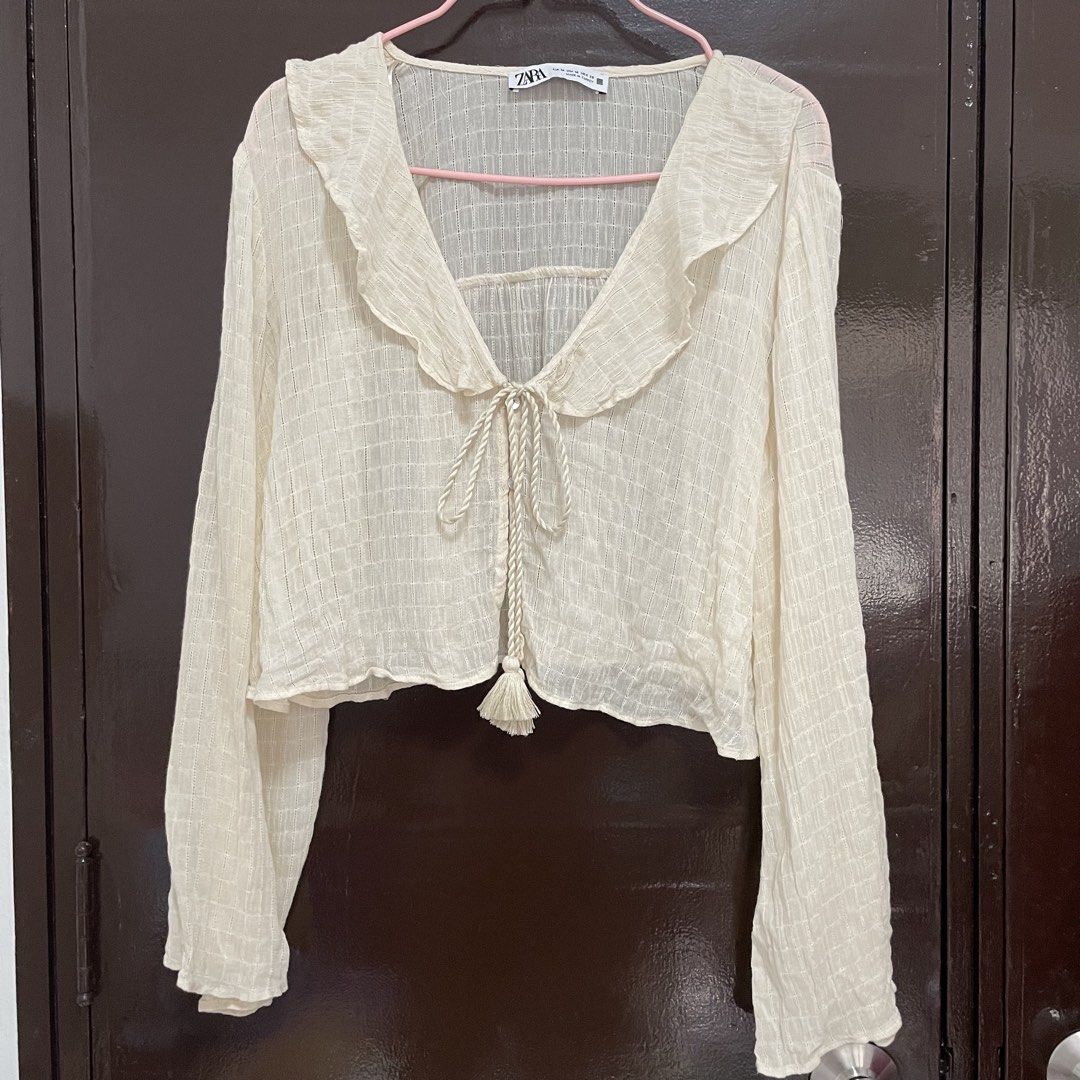 Zara Cream Ruffle Blouse Long Sleeve Size M (Category: Blouses) located in Pasay City. Submitted by lovedbyzea (Listing ID 1467338963, Image 1). Description: - SUPER NICE IN ACTUAL!! It’s sheer tho - Brand: Zara - Size: Medium (M) - Origin: Made in Turkey - Color: Cream - Design: Textured check pattern with ruffle collar and front tie-up closure with tassel strings - Fabric: Lightweight and slightly sheer - Condition: Excellent, wardrobe essentia