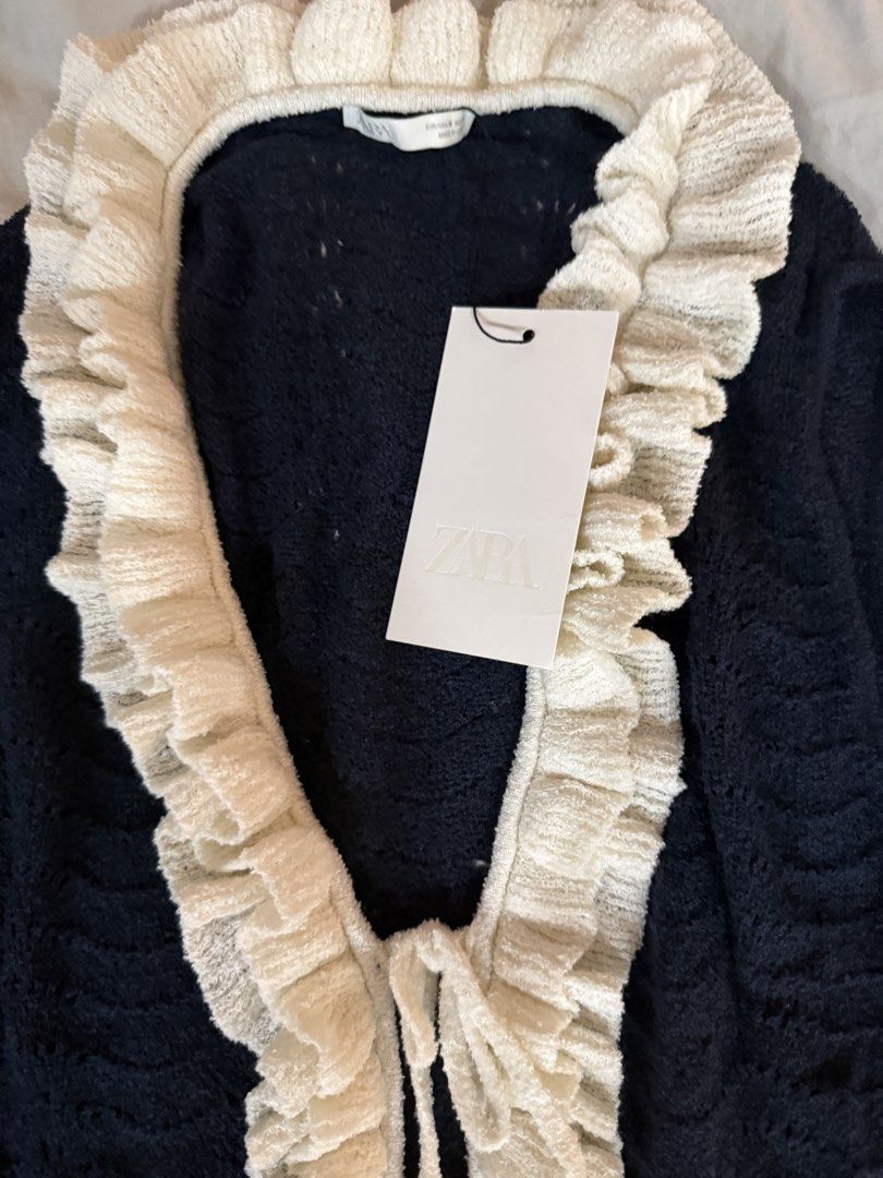 Zara Crochet Ruffled Vest (Category: Sleeveless) located in Pasig City. Submitted by atbp__ (Listing ID 1467213546, Image 3). Description: - Brand: Zara - Color: Dark navy blue with contrast white ruffled trim - Details: V-neckline, double front tie closure, sleeveless - Fabric: Textured open-weave knit - Condition: Brand new with original tag attached.
