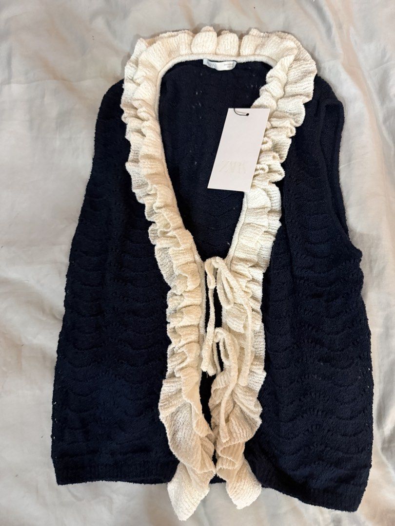 Zara Crochet Ruffled Vest (Category: Sleeveless) located in Pasig City. Submitted by atbp__ (Listing ID 1467213546, Image 2). Description: - Brand: Zara - Color: Dark navy blue with contrast white ruffled trim - Details: V-neckline, double front tie closure, sleeveless - Fabric: Textured open-weave knit - Condition: Brand new with original tag attached.