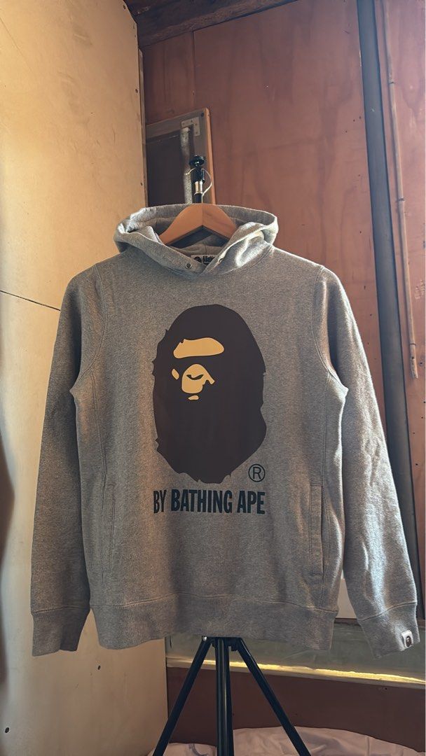 A Bathing Ape Grey Bape Head Hoodie (Category: Hoodies) located in Manila. Submitted by kobthrift.1223 (Listing ID 1467381100, Image 1). Description: - Authentic A Bathing Ape (Bape) grey hoodie - Classic brown Bape head logo and text print on chest - Cozy and warm fleece interior - Includes signature sleeve ape tag and neck tag - Features drawstring hood, front kangaroo pocket, and ribbed cuffs/hem.