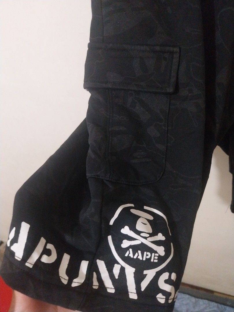 Aape Authentic Black Camo Cargo Shorts (Category: Shorts) located in Davao. Submitted by thegraildept2026 (Listing ID 1467547897, Image 2). Description: - Brand: Aape - Color: Black with subtle tonal camo print - Features: White graphic prints on hem and back pocket - Details: Metal Aape logo button, side cargo pockets, and Velcro patch with Aape text - Fit/Style: Drawstring eyelets along waistband, casual streetwear piece.