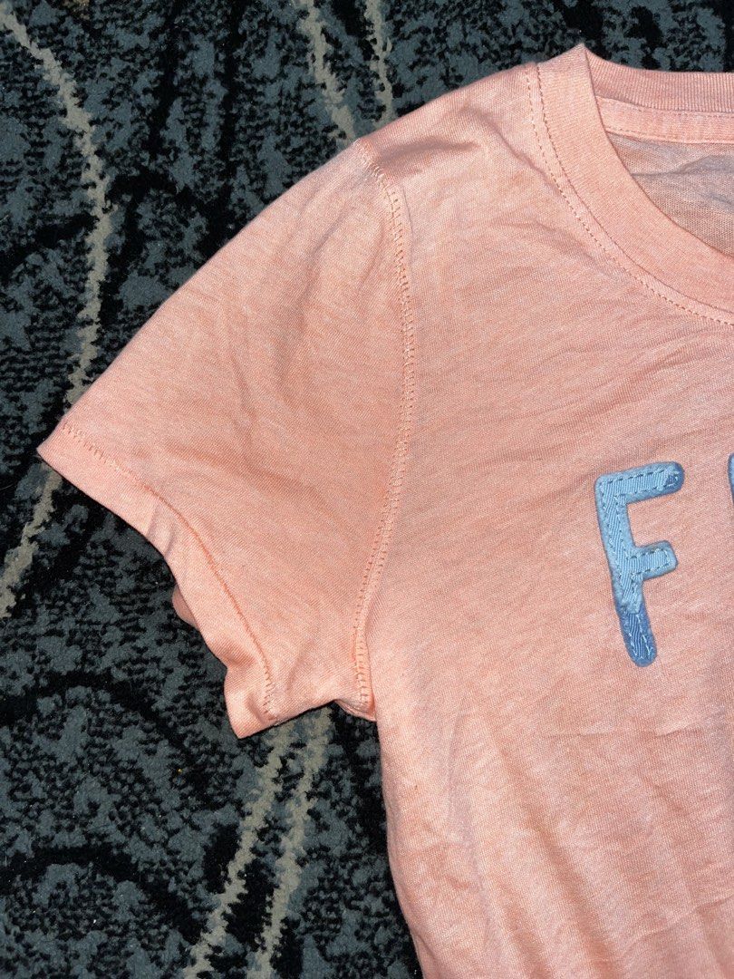Abercrombie & Fitch “Fitch” Shirt (Category: Shirts) located in Manila. Submitted by kashjulliane (Listing ID 1467366611, Image 3). Description: - Brand: Abercrombie & Fitch - Size: XS - Color: Pink with light blue 'FITCH' appliques - Material: Soft slub knit fabric - Design: Short sleeves, round neckline - Origin: Made in Cambodia - Condition: Excellent, casual everyday wear width 16 length 25.