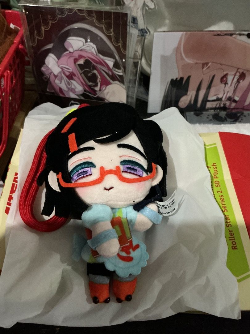 Alien stage roller star sua (Category: Plushies & Soft Toys) located in Aroroy. Submitted by douleur_y0u (Listing ID 1467397338, Image 1). Description: - Anime character plush hanging keychain - Features: Short black hair, purple eyes, and red-framed glasses - Outfit: Light blue top with apron, orange and black boots, and a small tag on the right arm - Extras: Attached red lanyard strap on the side.