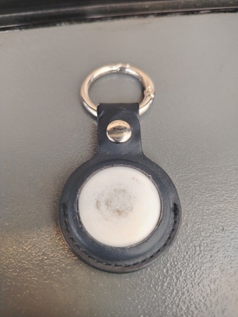 Apple AirTag with Black Leather Keychain Holder (Category: Cases & Sleeves) located in Manila. Submitted by dmab3005 (Listing ID 1467398745, Image 2). Description: - Authentic Apple AirTag tracker - Includes a black leather keychain case with a secure snap button and metal ring - Silver stainless steel backing with standard Apple logo - White plastic face features minor smudging from everyday use - 100% fully functional and ready to pair with iOS