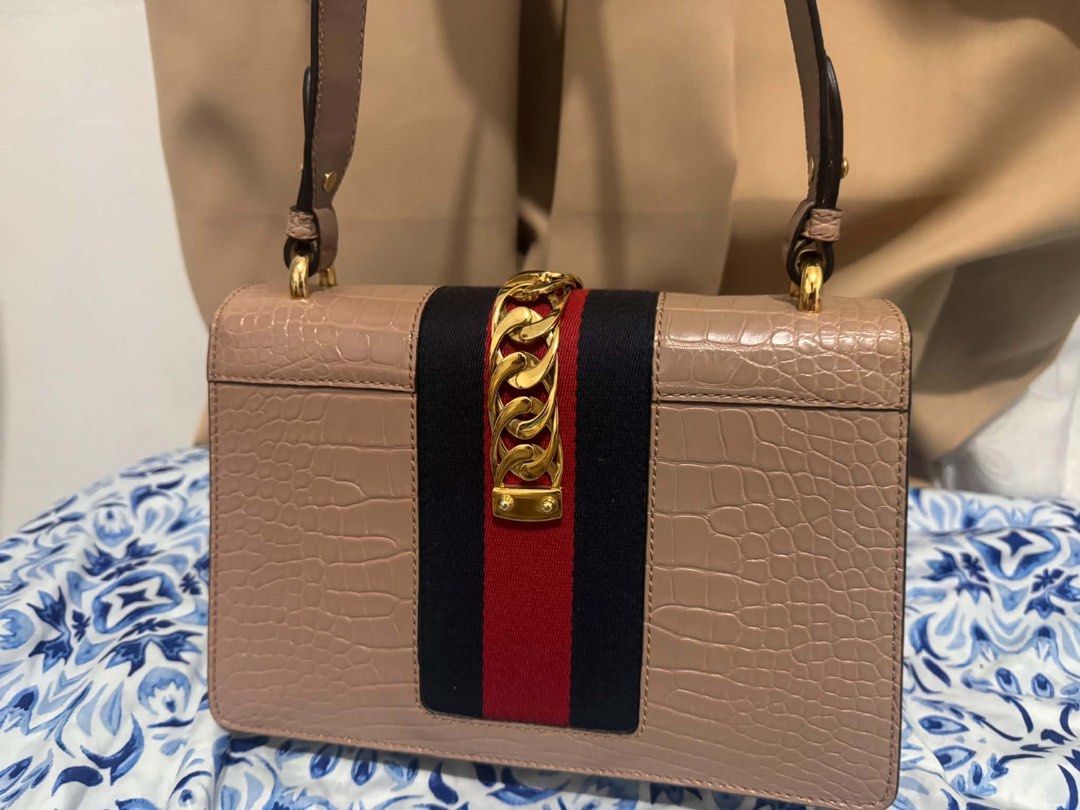 Authentic Gucci Sylvie Beige Exotic Crocodile Shoulder Bag (Category: Luxury Bags & Wallets) located in San Pedro. Submitted by rjgrat (Listing ID 1467423320, Image 2). Description: - Brand: Gucci - Style: Sylvie Shoulder Bag - Material: Beige exotic crocodile leather - Design: Signature navy and red web stripe with chunky gold-tone chain and buckle lock - Structure: Structured shape with a convenient top handle strap - Condition: Never used, goo