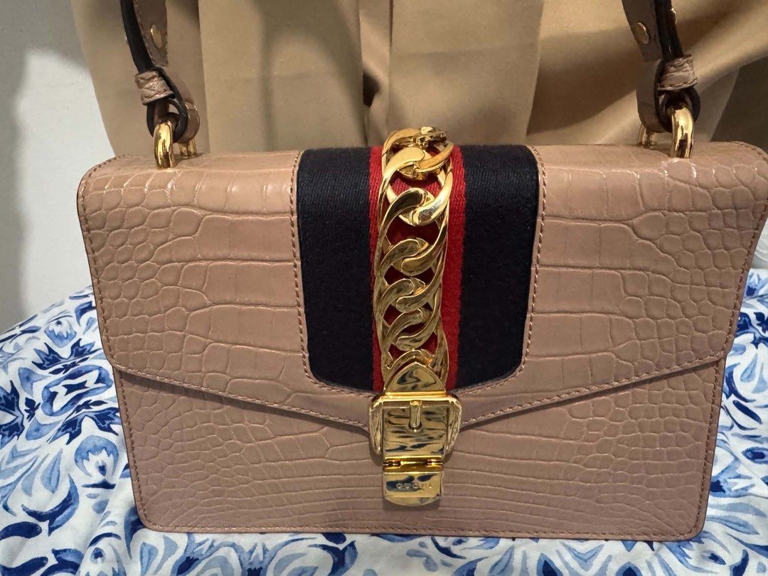 Authentic Gucci Sylvie Beige Exotic Crocodile Shoulder Bag (Category: Luxury Bags & Wallets) located in San Pedro. Submitted by rjgrat (Listing ID 1467423320, Image 1). Description: - Brand: Gucci - Style: Sylvie Shoulder Bag - Material: Beige exotic crocodile leather - Design: Signature navy and red web stripe with chunky gold-tone chain and buckle lock - Structure: Structured shape with a convenient top handle strap - Condition: Never used, goo