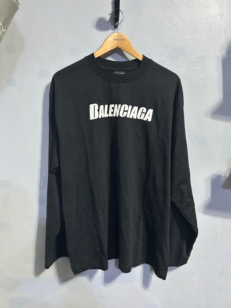Balenciaga Black Long Sleeve Tee Size L (Category: Luxury Apparel) located in Manila. Submitted by marjoriete27817 (Listing ID 1467523780, Image 1). Description: - Brand: Balenciaga - Color: Solid black - Size: L (Relaxed, oversized fit) 24*30 - Material: 100% cotton, made in Portugal - Design: Big white chest logo with slight cracking effect - Details: Ribbed crew neck with minor distressed collar detailing.