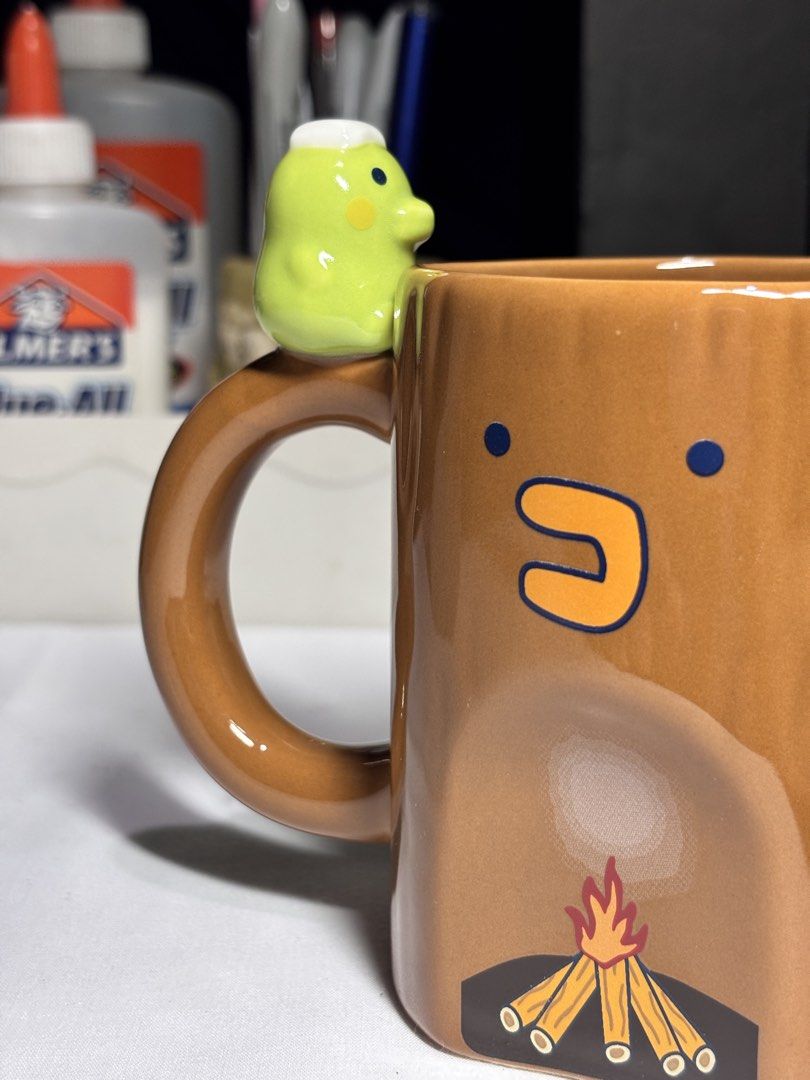 Bandai Namco Character Tree Trunk Ceramic Mug (Category: Coffee & Tea Tableware) located in Baguio. Submitted by 21enygrace.ph (Listing ID 1467481337, Image 2). Description: - Authentic Bandai Namco ceramic mug - Unique tree trunk design with brown gloss finish - Features a cozy campfire graphic on the front - Adorable small green character figure attached to the handle - Standard mug size that stands upright securely - Official stamp on the bott