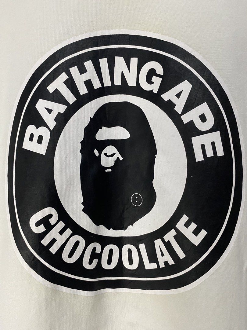 BATHING APE CHOCOLATE SHIRT (Category: Tshirts & Polo Shirts ) located in Jaen. Submitted by oshimamark58418 (Listing ID 1467537233, Image 3). Description: - Brand: Bathing Ape x Chocoolate - Color: White - Size: Large (Measured approx. 20" x 29") - Design: Bold circular BAPE ape head front graphic with typography - Style: Urban, casual, basic streetwear - Condition: Good quality pre-owned condition.