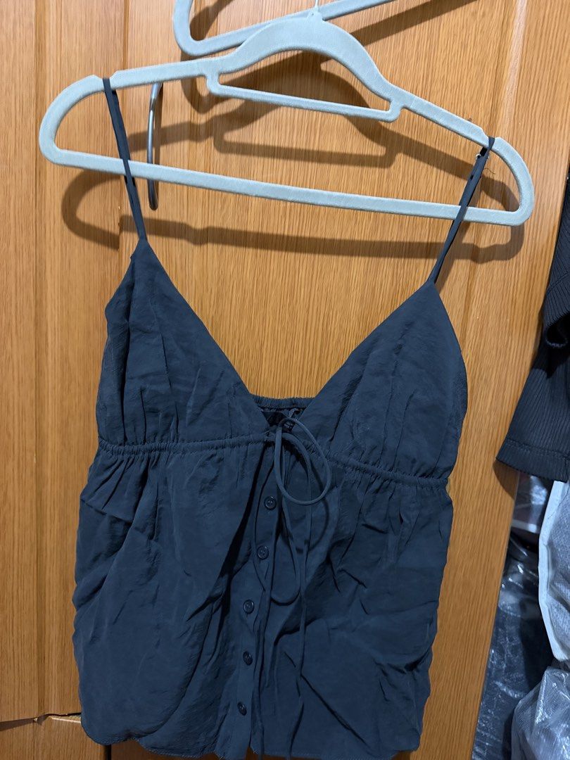 Black camisole with front buttons and ties (Category: Sleeveless) located in Muntinlupa City. Submitted by biancaagbscloset (Listing ID 1467515962, Image 1). Description: - Color: Dark Grey - Style: V-neck camisole with thin spaghetti straps and center front buttons - Detail: Cute middle tie string and gathered elastic under-bust for a flattering, flowy hem - Fabric: Lightweight with a nice crinkle texture - Condition: Brand new / Excellent - Mod
