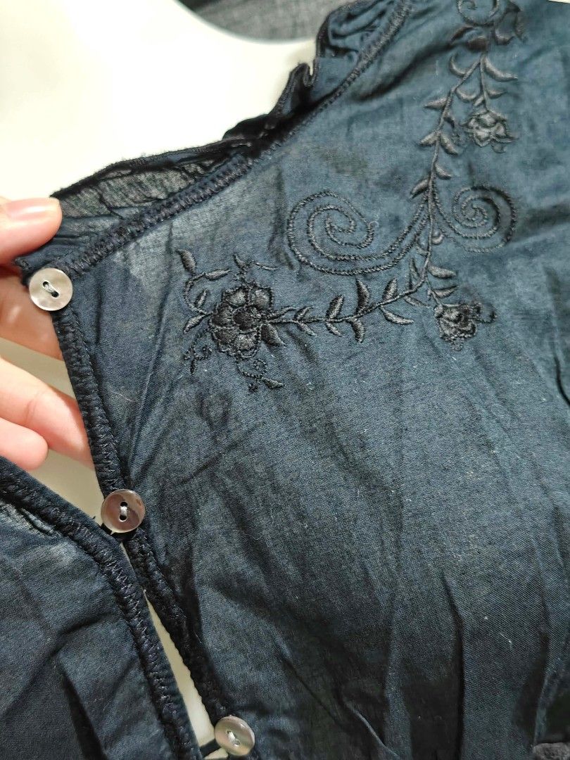 Black embroidered button-down blouse with tie waist (Category: Blouses) located in Quezon City. Submitted by cleocastillo_262 (Listing ID 1467382680, Image 2). Description: - Color: Dark green or black - Design: Button-down front with delicate floral embroidery on neckline and shoulders - Fit: Adjustable tie string at the waist - Details: Ruffle trim on collar and cuffs - Fabric: Lightweight, breathable, and textured material - Condition: Brand n