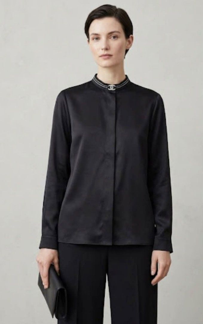 Black Silk Blouse with embellished collarline (Category: Blouses) located in Donsol. Submitted by saksthriftavenuebyluckymaria8 (Listing ID 1467383893, Image 2). Description: - Material: Smooth luxury silk - Color: Classic black - Design: High collar with silver beading and logo at neckline - Details: Long sleeves : Tailored, timeless wardrobe staple - Condition: Excellent Black blouse features a band/mandarin collar accented with a jeweled ogo b