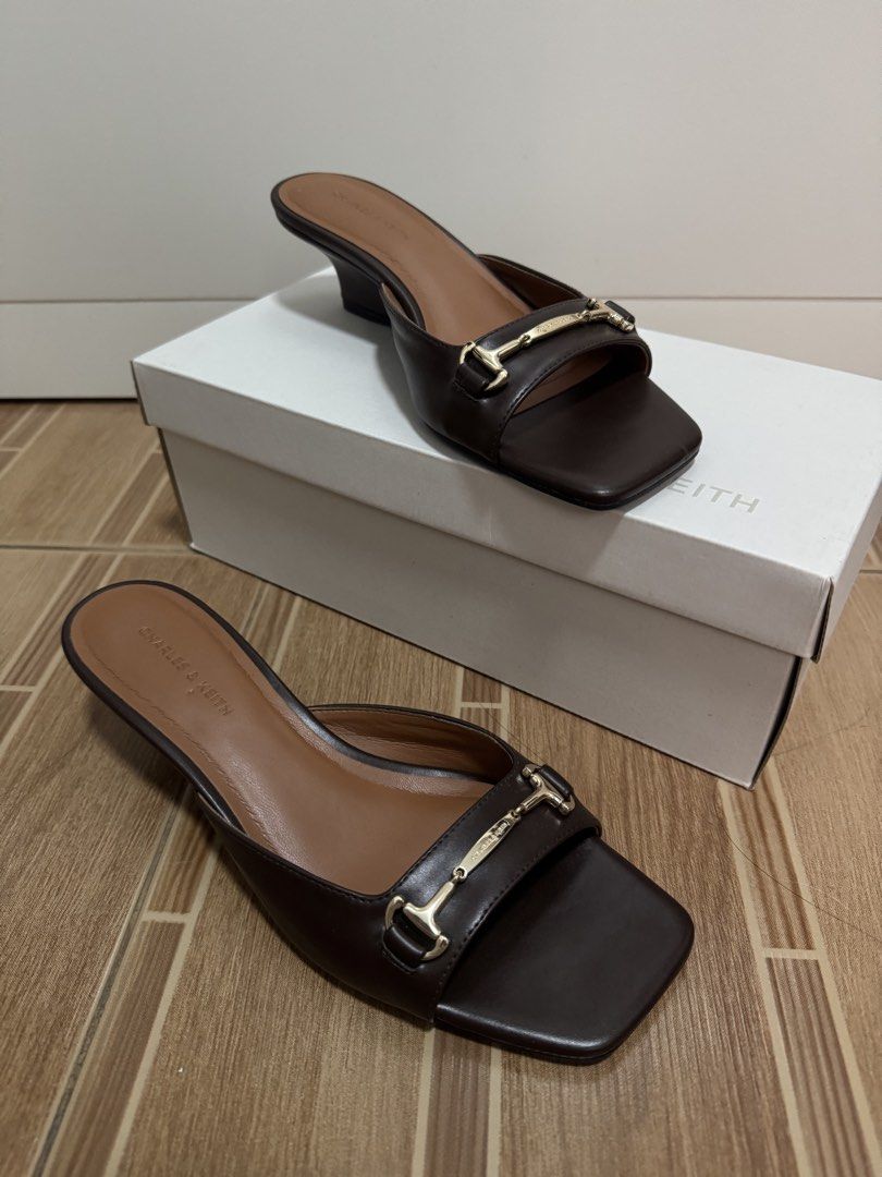 Charles & Keith Dark Brown Mules Size 37 (Category: Flats & Sandals) located in Manila. Submitted by dianesls_13 (Listing ID 1467413099, Image 1). Description: - Brand: Charles & Keith - Model: Erinna Mules - Color: Dark Brown - Size: EU 37 - Heel Style: Wedge heel with square toe design - Accent: Elegant gold-tone hardware detail across the strap - Inclusions: Comes with original shoe box and paper bag - Condition: Excellent/As seen in pictures.