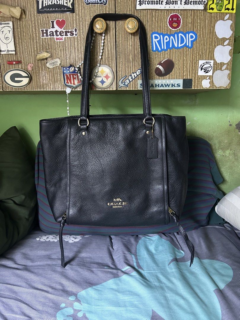Coach Black Leather Tote Bag (Category: Tote Bags) located in Quezon City. Submitted by thriftxgoods (Listing ID 1467440646, Image 1). Description: Coach black pebble leather tote bag. Gold hardware details and front logo lettering. Dual shoulder straps, zip top closure, roomy black fabric interior with zip pocket. Leather hang tag attached. Interior creed patch shows peeling surface finish..