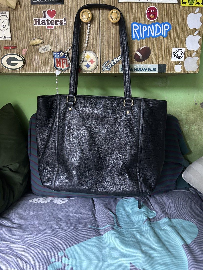 Coach Black Leather Tote Bag (Category: Tote Bags) located in Quezon City. Submitted by thriftxgoods (Listing ID 1467440646, Image 3). Description: Coach black pebble leather tote bag. Gold hardware details and front logo lettering. Dual shoulder straps, zip top closure, roomy black fabric interior with zip pocket. Leather hang tag attached. Interior creed patch shows peeling surface finish..
