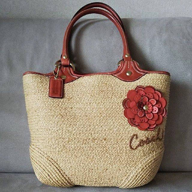 Coach Bleecker Straw / Leather Flower Tote Bag (Category: Shoulder Bags) located in Bacacay. Submitted by curatedsbyjj (Listing ID 1467523684, Image 1). Description: Coach Bleecker straw and leather tote bag featuring a decorative flower applique, sturdy leather handles, and a spacious red fabric interior with organizational pockets. Shows minor wear on the handles, but overall in good pre-loved condition. Perfect for casual wear and vacations. >