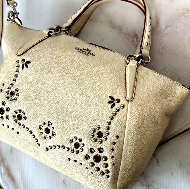 Coach White Leather Studded Satchel Bag (Category: Cross-body Bags) located in Manila. Submitted by lene48 (Listing ID 1467382494, Image 1). Description: - Authentic Coach pebbled leather handbag in cream white - Features gorgeous metal studs and gemstones in floral patterns on the front - Silver-tone hardware and matching Coach leather hangtag included - Versatile styling: use the top handle or attach the strap for crossbody/shoulder wear - Clea