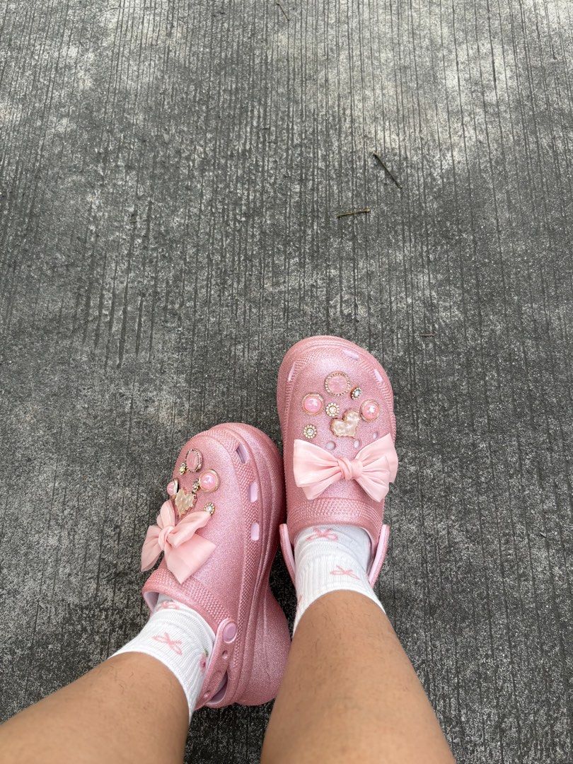 Crocs pink glitter clogs (Category: Flats & Sandals) located in Taytay. Submitted by barbiemilli (Listing ID 1467416452, Image 2). Description: - Style: Fun coquette aesthetic, glittery pink platform clogs - Details: Decorated with pearl and rhinestone charms plus a large front satin ribbon bow - Sole: Chunky platform for extra height - Inclusions: Comes with white socks featuring tiny pink ribbon prints - Condition: Brand new / Excellent quality