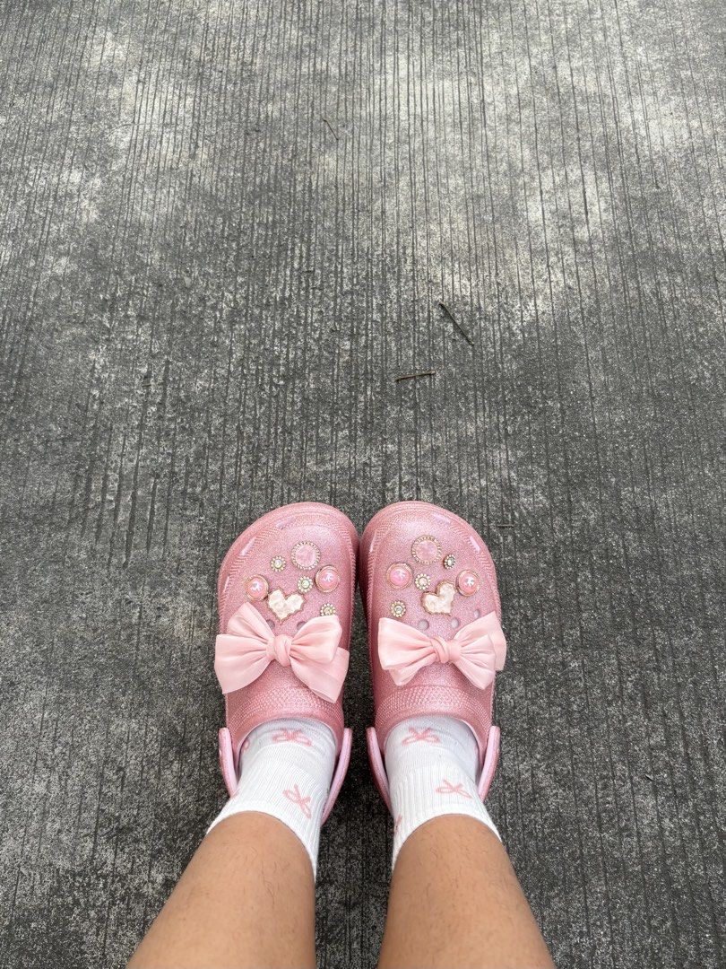 Crocs pink glitter clogs (Category: Flats & Sandals) located in Taytay. Submitted by barbiemilli (Listing ID 1467416452, Image 1). Description: - Style: Fun coquette aesthetic, glittery pink platform clogs - Details: Decorated with pearl and rhinestone charms plus a large front satin ribbon bow - Sole: Chunky platform for extra height - Inclusions: Comes with white socks featuring tiny pink ribbon prints - Condition: Brand new / Excellent quality