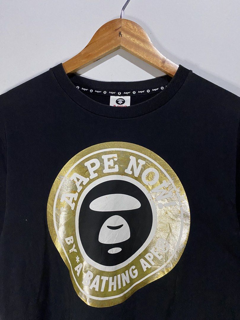 CROP AAPE SHIRT (Category: Others Tops) located in Jaen. Submitted by oshimamark58418 (Listing ID 1467536449, Image 2). Description: - Brand: Aape by A Bathing Ape - Style: Crop T-shirt / Streetwear top - Color: Black with gold and white graphic print ('Aape Now!') - Size: XXS (Measurements: 19x19 inches, fits like Small) - Features: Branded collar tape and sleeve logo tags - Condition: Good pre-owned condition.
