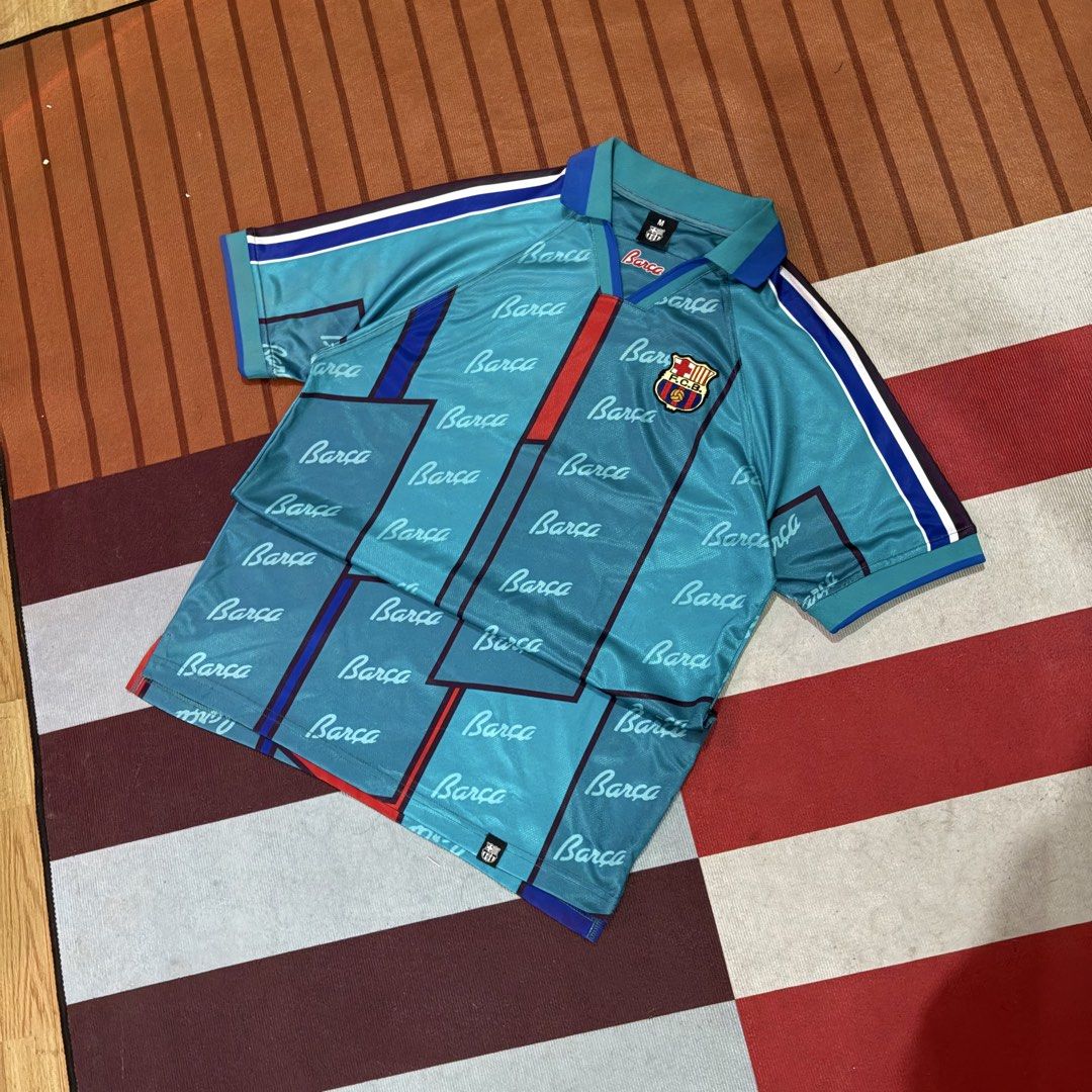 FC Barcelona Blue Retro Jersey (Category: Activewear) located in Manila. Submitted by carlmachu (Listing ID 1467495879, Image 1). Description: - Item: Vintage FC Barcelona Football Jersey - Color: Teal blue with blocking stripes - Design: All-over repeating 'Barça' script pattern - Details: Classic polo collar with button placket, woven club crest patch, and striped sleeve trim - Size: Medium (M) - Condition: Excellent vintage style - Perfect for