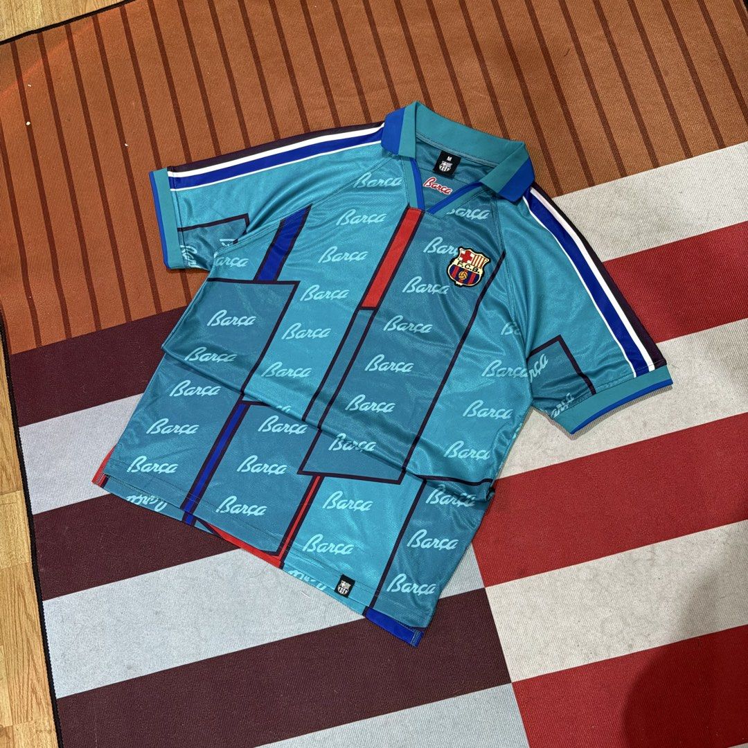 FC Barcelona Blue Retro Jersey (Category: Activewear) located in Manila. Submitted by carlmachu (Listing ID 1467495879, Image 2). Description: - Item: Vintage FC Barcelona Football Jersey - Color: Teal blue with blocking stripes - Design: All-over repeating 'Barça' script pattern - Details: Classic polo collar with button placket, woven club crest patch, and striped sleeve trim - Size: Medium (M) - Condition: Excellent vintage style - Perfect for