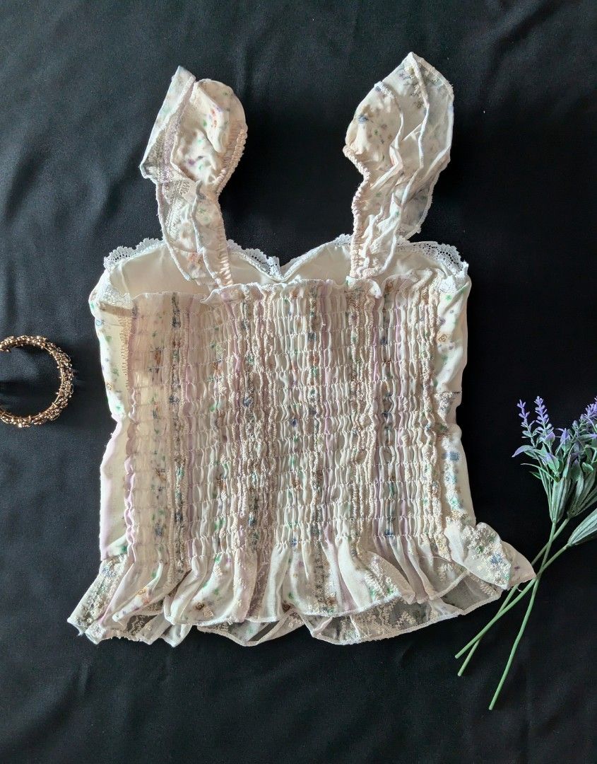 Floral Ruffle Strap Cami Top with Back Smocking (Category: Sleeveless) located in Kananga. Submitted by aurylien.clo (Listing ID 1467467696, Image 2). Description: - XS-M - Cream floral cami top with pastel colors and vertical striped panels - Sweetheart neckline featuring a cute light purple center ribbon tie - Playful ruffle shoulder straps and ruffled hemline with delicate lace trim - Fully smocked back panel for a flexible, comfortable stretc