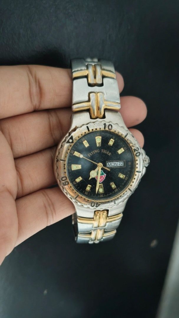 Flying Tiger Two Tone Quartz Wristwatch (Category: Men's Watches) located in Taguig. Submitted by mercyeugen28914 (Listing ID 1467451463, Image 2). Description: - Brand: Preloved Flying Tiger - Movement: Quartz - Dial: Black with gold hour markers and 3 o'clock day/date window - Bezel: not Rotating bezel with numbers - Bracelet: Two-tone silver and gold stainless steel link bracelet - Condition: Visible scratches on the case, bezel, and band from