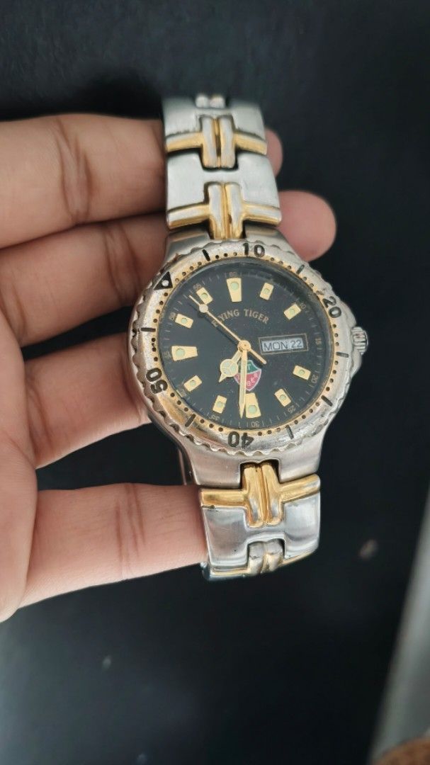 Flying Tiger Two Tone Quartz Wristwatch (Category: Men's Watches) located in Taguig. Submitted by mercyeugen28914 (Listing ID 1467451463, Image 3). Description: - Brand: Preloved Flying Tiger - Movement: Quartz - Dial: Black with gold hour markers and 3 o'clock day/date window - Bezel: not Rotating bezel with numbers - Bracelet: Two-tone silver and gold stainless steel link bracelet - Condition: Visible scratches on the case, bezel, and band from